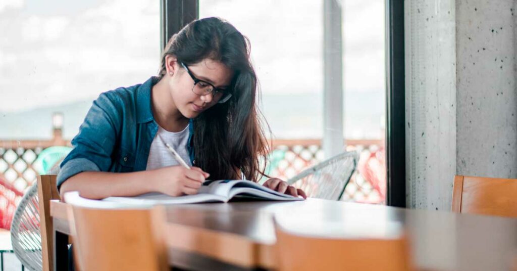 Menina estudando, escrevendo em caderno em cima da mesa